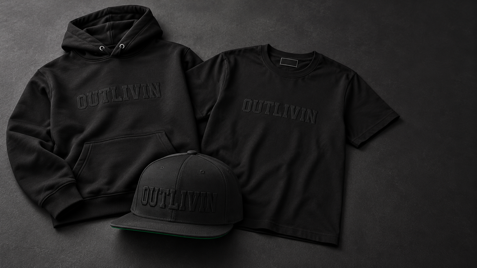 OUTLIVIN black-on-black hoodie, heavyweight T-shirt, and 3D puff snapback together on a charcoal background